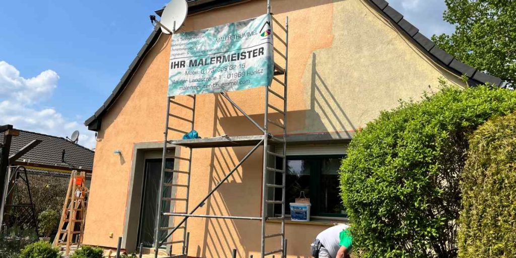 Zu der Fassadengestaltung: Rüstung mit Firmen Banner am Giebel.